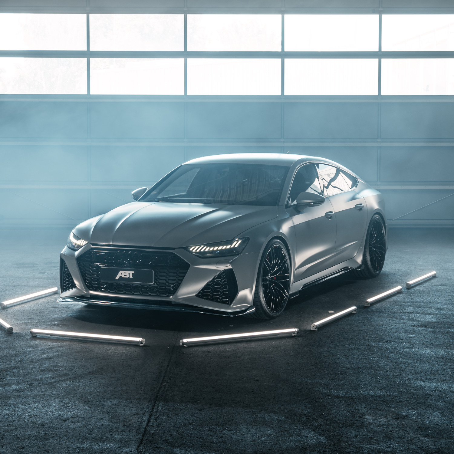 grey ABT RS7-S from the side front view illuminated by LED bars in warehouse in front of gate 