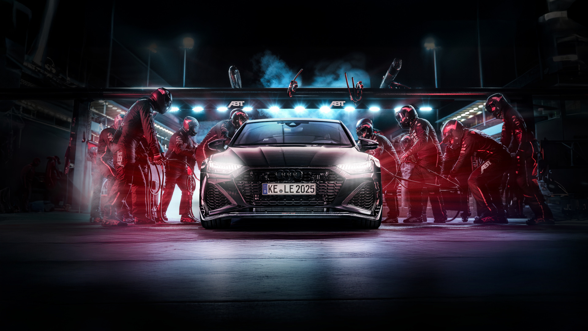 Black RS6-LE from the front view during a pit stop on the racetrack with a team around it 